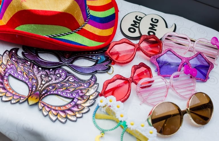 Colorful party accessories including novelty sunglasses, feathered masks, rainbow sombrero, and beaded necklaces