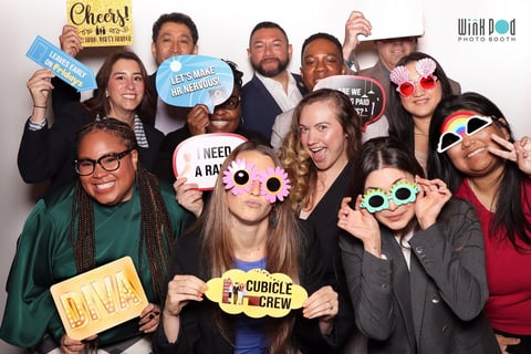 Group of people at a photo booth event wearing silly glasses and holding fun props and signs