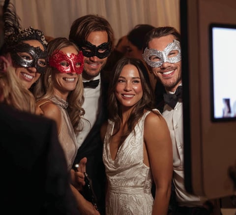 Group of elegantly dressed people wearing decorative masquerade masks at an indoor formal event