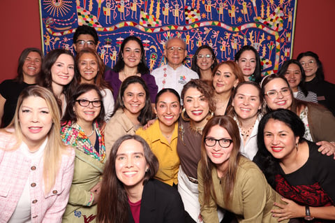 Group of diverse women posing together in front of a decorative blue and gold tapestry on a red wall