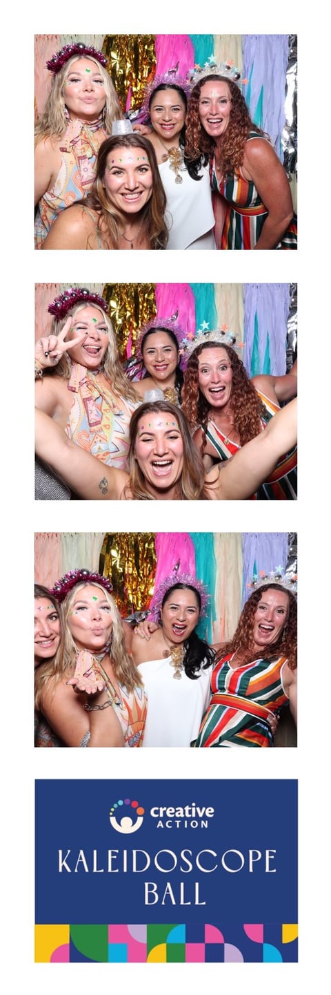 Four women posing for photos at a colorful Kaleidoscope Ball event, wearing festive outfits and accessories against a vibrant streamer backdrop
